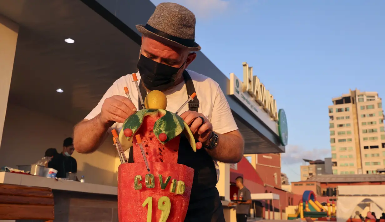 Koki Suriah Wareef Qassem memberikan sentuhan akhir pada semangka berukir yang mengajak orang-orang untuk divaksinasi terhadap Covid-19, di Kota Gaza (13/7/2021). (AFP/Mohammed Abed)
