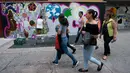 Sekelompok wanita berjalan melewati seniman grafiti Sandra Fabara atau lebih dikenal Lady Pink yang tengah melukis mural di Casita Maria, Bronx, New York, AS, Minggu (2/6/2019). Di usianya yang sudah menginjak 50 tahun, Lady Pink mencari nafkah dengan karya seninya secara legal. (Don Emmert/AFP)