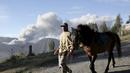 Seorang pria sambil menuntun kuda miliknya berjalan dengan latar belakang semburan abu vulkanik dari Gunung Bromo yang sedang erupsi di Ngadisari, Probolinggo, Jawa Timur, Rabu (6/1/2016). (REUTERS/Darren Whiteside)