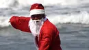 Seorang pria berkostum Santa Claus berselancar di Pantai Kuta, Bali, Senin (10/12). Setiap tahunnya, ribuan wisatawan mendatangi Bali saat menjelang natal dan tahun baru. (AFP PHOTO / Sonny Tumbelaka)