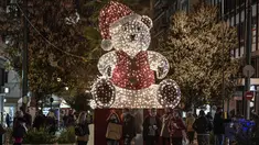 Orang-orang berdiri di dekat beruang raksasa yang diterangi dengan dekorasi Natal di jalan komersial utama Athena, Yunani pada 21 Desember 2020. Yunani akan merayakan musim Natal di bawah penguncian wilayah atau lockdown akibat virus corona hingga 7 Januari 2021 mendatang. (LOUISA GOULIAMAKI/AFP)
