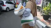 Warga berjalan dengan membawa beras kemasan 10 kilogram di Kelurahan Pela Mampang, Jakarta, Jumat (3/5/2024). (merdeka.com/Imam Buhori)