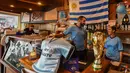 Bendera Uruguay, replika trofi Piala Dunia dan jersey ditampilkan di bar di Montevideo (4/7). Warga Uruguay antusias mempersiapkan untuk mendukung negaranya bertanding melawan Prancis pada babak 8 besar Piala Dunia 2018 di Rusia. (AFP Photo/Miguel Rojo)