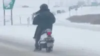 Seorang pria mengendarai skuter saat kondisi cuaca dingin akibat badai salju di sebuah jalan di Calgary, Kanada.