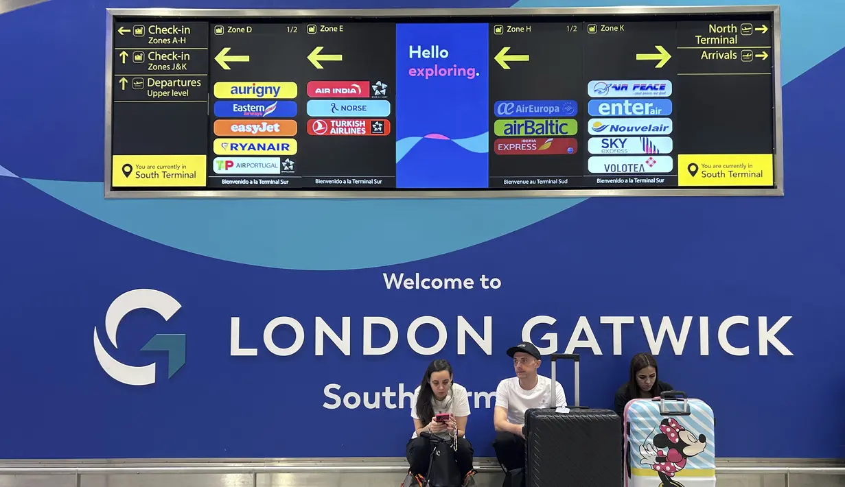 Para penumpang duduk di depan papan informasi yang menunjukkan lokasi meja maskapai di Bandara Gatwick dekat London, Inggris, Kamis 12 Juni 2025. (AP/Kin Cheung)