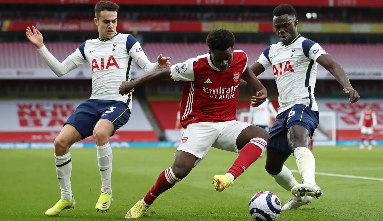 Striker Arsenal Bukayo Saka (tengah) bersaing memperebutkan bola dengan pemain Tottenham Hotspur Sergio Reguilon (kiri) dan Davinson Sanchez dalam derby London Utara Liga Inggris di Emirates Stadium, Minggu (14/3/2021). Sempat tertinggal, Arsenal menang 2-1 atas Tottenham. (Nick Potts/POOL/AFP)