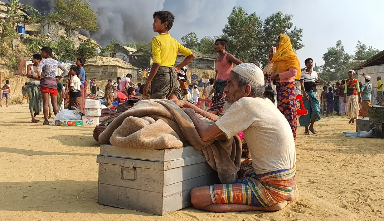 Pengungsi Rohingya menyelamatkan barang-barang mereka dan menyaksikan asap membubung menyusul kebakaran di kamp pengungsi Rohingya di Balukhali, Bangladesh selatan (22/3/2021). Kebakaran tersebut diperkirakan menghancurkan 900 tenda tempat ribuan pengungsi berlindung. (AP Photo/Shafiqur Rahman)