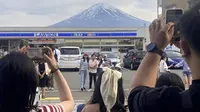 Para pengunjung mengambil foto di depan toko serba ada di kota Fujikawaguchiko, prefektur Yamanashi, Jepang, dengan latar belakang Gunung Fuji pada tanggal 28 April 2024. (Kyodo News via AP)