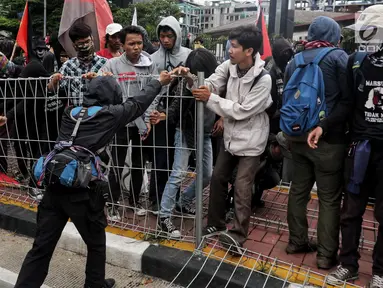 Peserta aksi dari berbagai serikat buruh berusaha merobohkan pagar besi di pelican crossing Tosari saat peringatan Hari Buruh 2019 di Jalan Jenderal Sudirman dekat Bundaran HI, Jakarta, Rabu (1/5/2019). Pagar roboh terdorong massa May Day yang merangsek barikade polisi. (Liputan6.com/Johan Tallo)