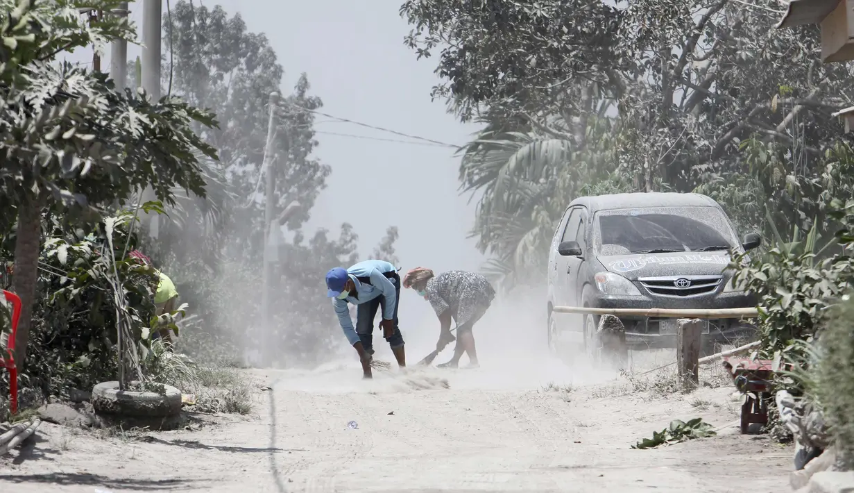 Warga mengenakan masker membersihkan jalan yang tertutup abu vulkanik Gunung Sinabung di Karo, Sumatra Utara (20/2). Gunung Sinabung meletus kembali tanggal 19 Februari, yang mengeluarkan asap tebal setinggi 5.000 meter. (AFP Photo/Kadri Boy Tarigan)
