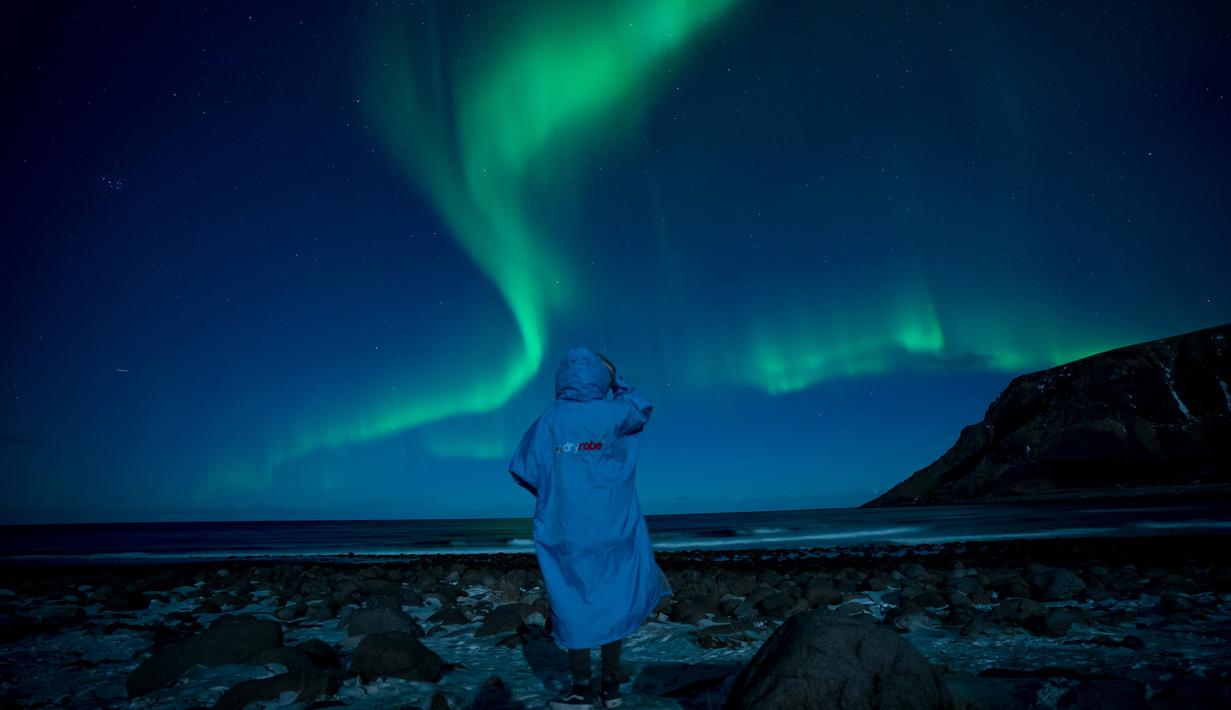 Seseorang menonton fenomena alam Aurora Borealis atau Northern Lights di Unstad, lingkaran Arktik, Norwegia, Sabtu (3/3). Aurora menampilkan banyak warna, tapi yang sering muncul adalah hijau muda dan pink. (Olivier MORIN/AFP)