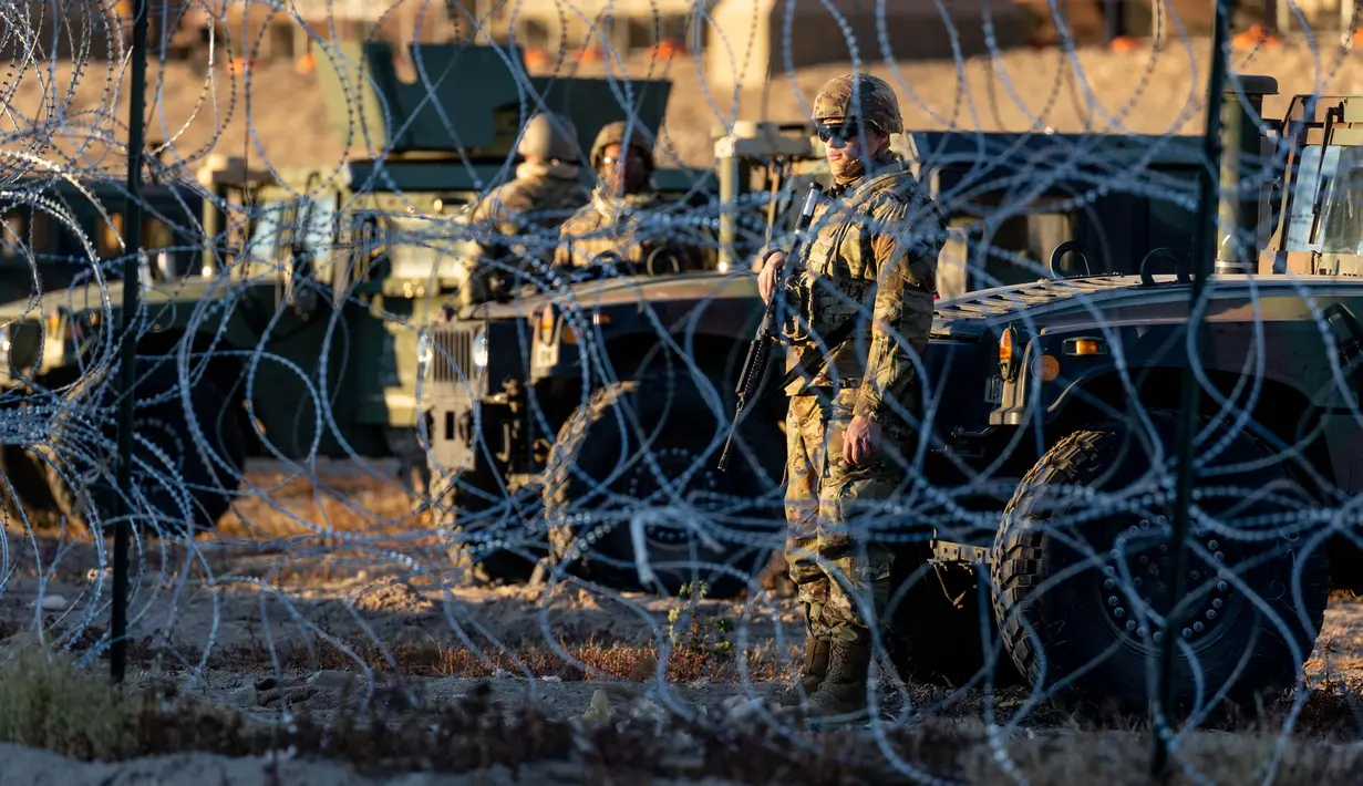 Tentara Pengawal Nasional Texas berjaga di belakang kawat berduri di perbatasan AS-Meksiko, Ciudad Juarez, Meksiko, Rabu (21/12/2022). Kebijakan Judul 42 ini dilakukan Trump untuk menghentikan penyebaran virus Corona dan memungkinkan AS mengusir hampir semua orang yang tertangkap melewati perbatasan secara ilegal. (JOHN MOORE / GETTY IMAGES NORTH AMERICA / Getty Images via AFP)