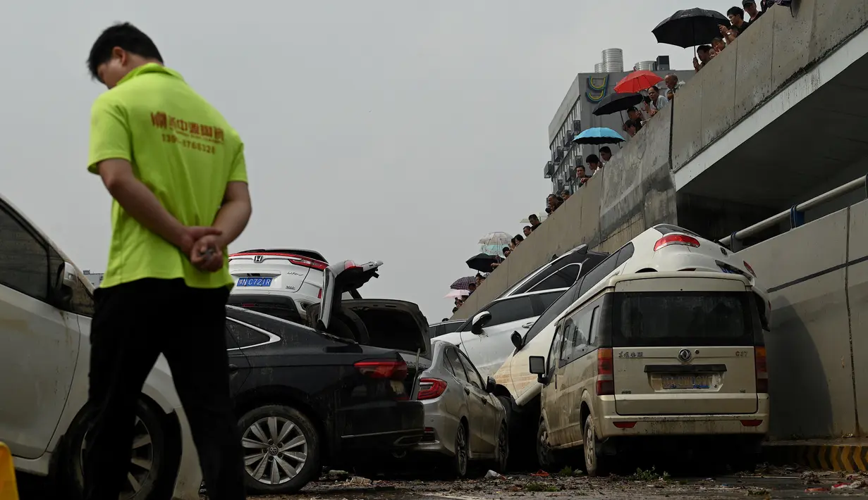 Orang-orang melihat mobil-mobil yang terendam banjir setelah hujan lebat melanda Zhengzhou di provinsi Henan, Kamis (22/7/2021). Henan, provinsi terbesar ketiga di China, yang merupakan rumah bagi sekitar 94 juta orang, telah dilanda badai hujan yang tidak biasa sejak akhir pekan. (Noel Celis/AFP)