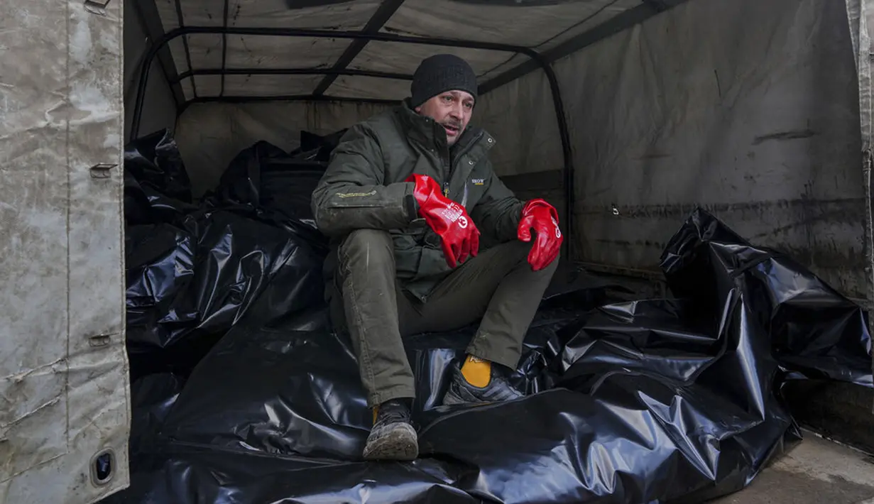 Seorang pekerja kamar jenazah duduk di atas kantong jenazah sebelum diangkut untuk dimakamkan di kuburan massal di pinggiran Mariupol, Ukraina, 9 Maret 2022. (AP Photo/Evgeniy Maloletka)