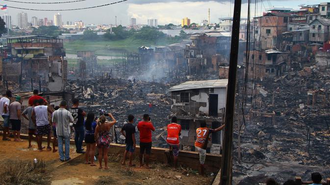 Sejumlah warga melihat sisa-sisa rumah yang hangus di lingkungan Educandos di Manaus, Brasil (17/12). Para pihak berwenang mengatakan setidaknya 600 rumah kayu hangus terbakar. (AP Photo/Edmar Barros)