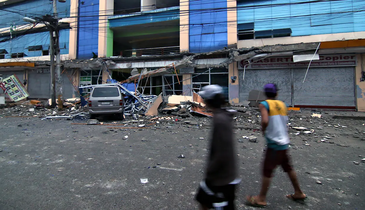 Warga berjalan melewati sebuah mobil yang tertimpa puing bangunan runtuh akibat gempa 6,5 SR yang melanda Surigao City, Pulau Mindanao, Filipina (11/2). (AFP/Erwin Mascarinas)