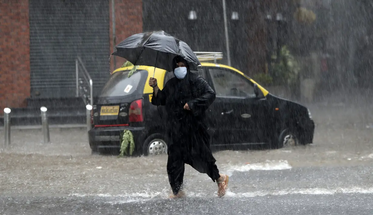 Seorang wanita mengenakan masker sebagai tindakan pencegahan terhadap virus corona melintasi banjir saat hujan lebat di Mumbai, India, Rabu, (5/8/2020). Musim hujan India berlangsung dari Juni hingga September. (AP Photo/Rajanish Kakade)