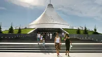 Penduduk lokal Kazakhstan berjalan di dekat tenda Khan Shatyr yang baru di Astana pada tanggal 14 Juli 2010. Arsitek Inggris Foster and Partners telah merancang kompleks perbelanjaan dan hiburan Khan Shatyr yang baru di Astana sebagai tenda besar, setinggi 100 meter (330 kaki) dari dasar ke atas dan 150 meter (500 kaki) termasuk tiang di atasnya. (Dok: AFP / STANISLAV FILIPPOV)