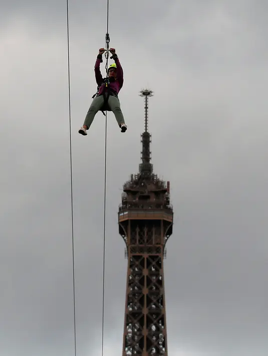 Pengunjung meluncur dengan seutas tali saat melakukan permainan Zip Line dari lantai dua Menara Eiffel di atas taman Champ de Mars, Paris, Selasa (28/5/2019). Permainan ini akan membiarkan pengunjung terbang di atas kerumunan turis di Champs de Mars sebelum mendarat dengan selamat (AP/Francois Mori)