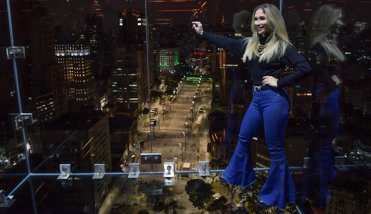 Seorang pengunjung berpose di Sampa Sky Observation Deck di Sao Paulo, Brasil pada 05 Agustus 2021. Pengunjung akan merasakan sensasi mendebarkan sekaligus menguji adrenalin berdiri di lantai transparan di ketinggian. (NELSON ALMEIDA / AFP)