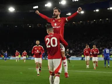 Gelandang Manchester United, Bruno Fernandes melompat ke pelukan Diogo Dalot saat merayakan gol ketiga mereka pada pertandingan pekan ke-29 Premier League 2024/2025 melawan Leicester City di King Power Stadium, Inggris pada 16 Maret 2025 waktu setempat atau Senin (17/3/2025) dini hari WIB. (Adrian Dennis/AFP)