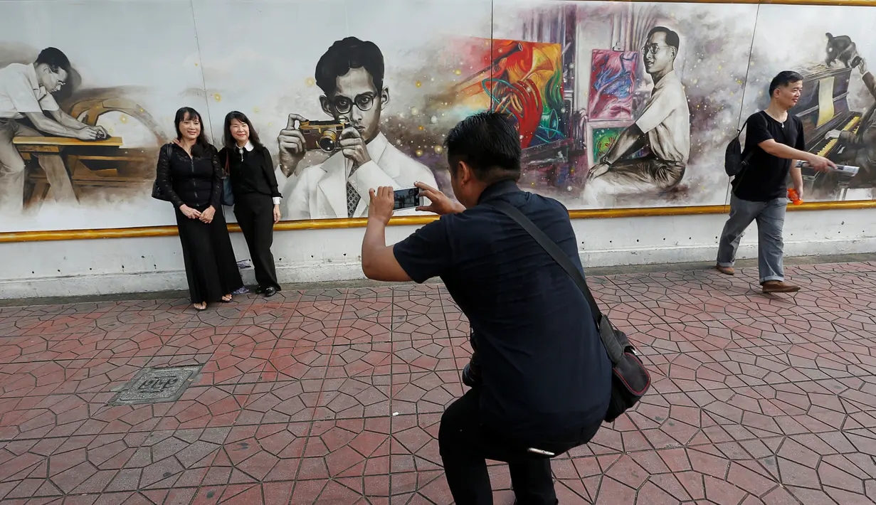 Sejumlah pengunjung berpose di dekat gambar Raja Bhumibol Adulyadej yang terpasang di Grand Palace di Bangkok, Thailand, Rabu (19/10). Untuk menghormati Raja Bhumibol Adulyadej, Grand Palace dipasangi gambarnya. (REUTERS / Chaiwat Subprasom)