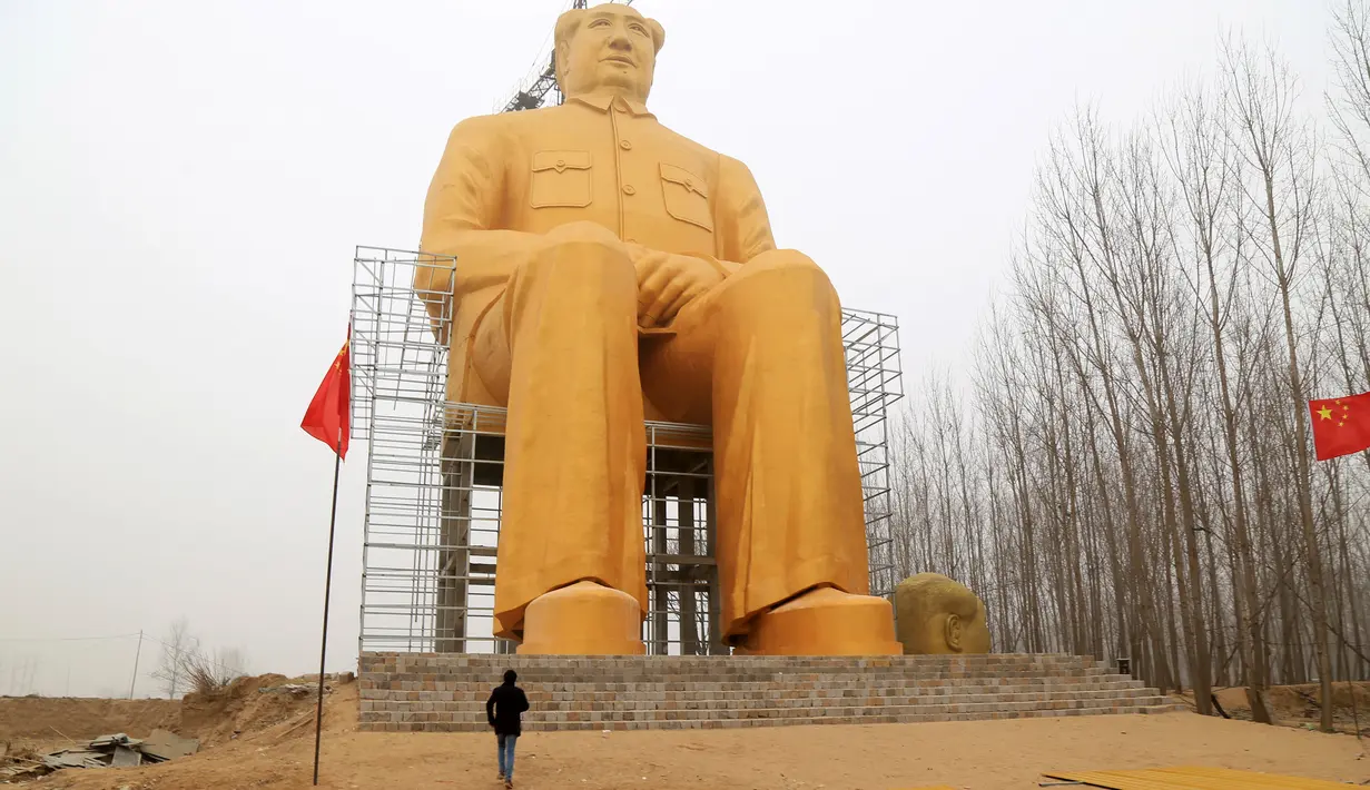 Seorang pria berada dibawah patung Presiden pertama Cina, Mao Zedong saat proses penyelesaian pembangunannya di ladang Desa Tongxu, Henan, Cina (4/1). Menurut warga, patung tersebut menghabiskan sekitar USD 460.000 atau Rp 6,4 miliar. (Reuters/Stringer)