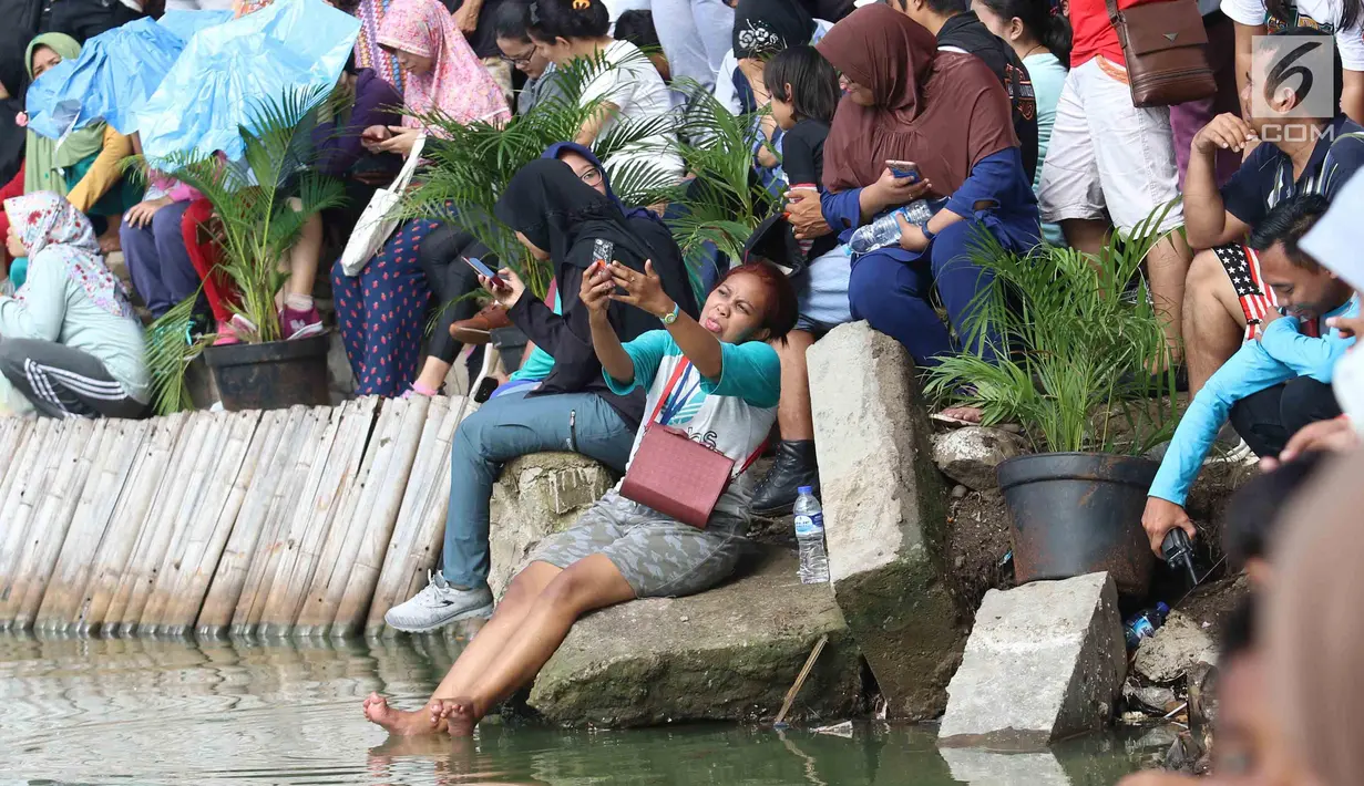 Seorang warga berselfie saat menyaksikan pertandingan antara Menteri KKP Susi Pudjiastuti dan Wagub DKI Jakarta Sandiaga Uno mengarungi danau sunter selama Festival Danau Sunter di Jakarta, Minggu (25/2). (Liputan6.com/Angga Yuniar)