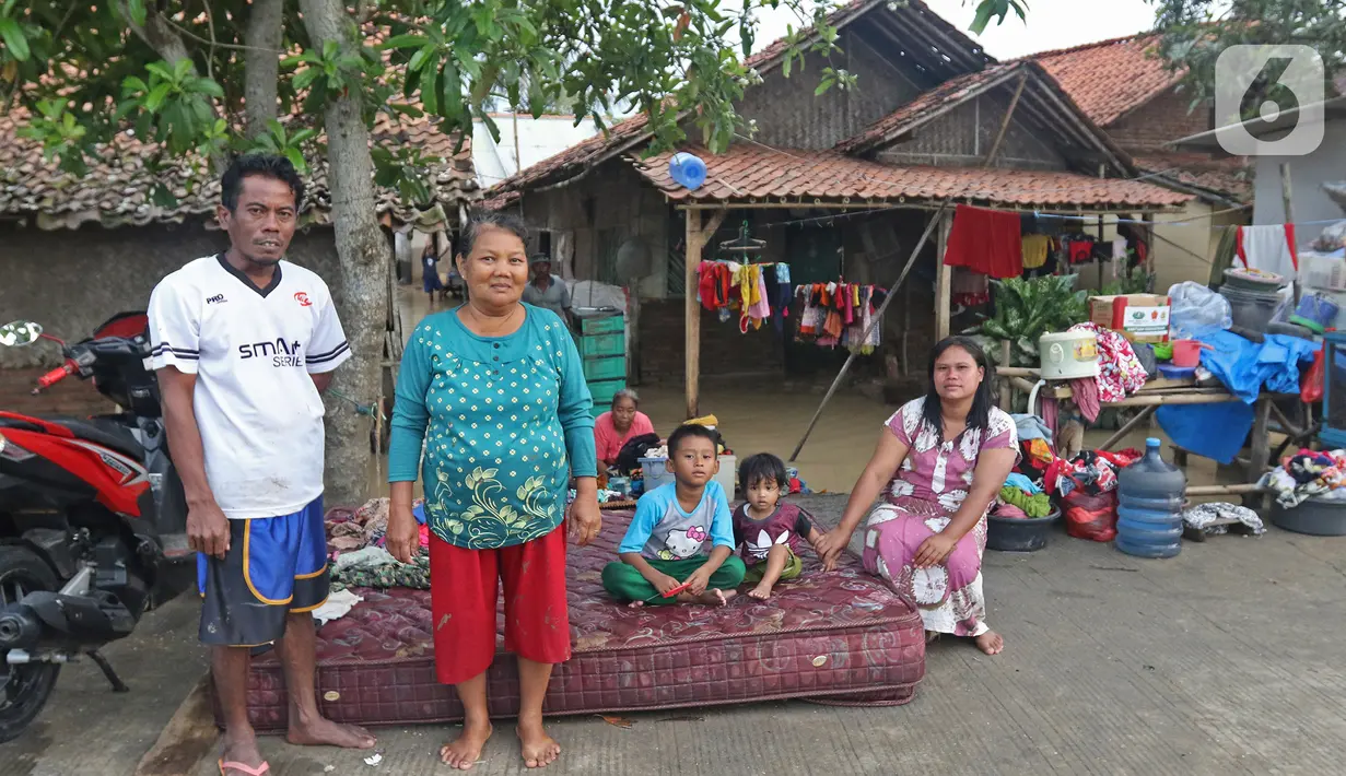 Keluarga Pak Piat berpose di depan kediamannya Desa Sumber Urip Pebayuran, Kabupaten Bekasi, Jawa Barat, Senin (22/2/2021). Banjir merenda keluarga tersebut merapikan barang-barang dan bersihkan rumah yang sudah surut. (Liputan6.com/Herman Zakharia)