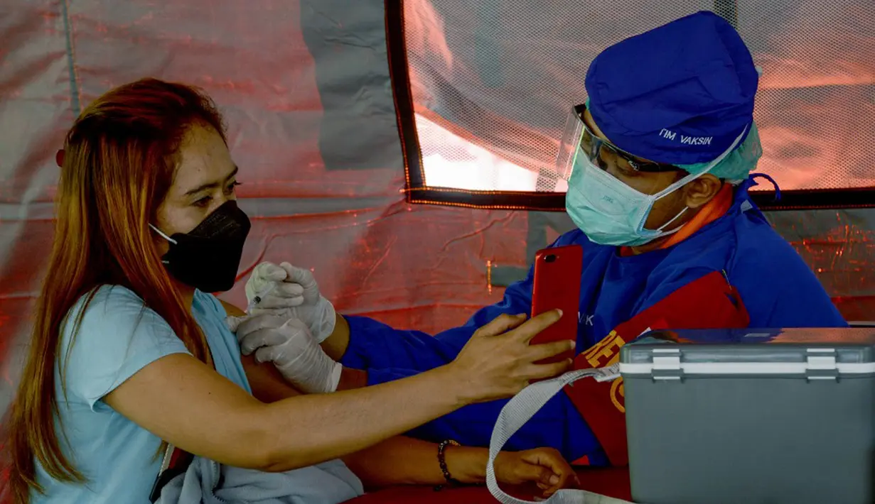 Seorang wanita menerima vaksin virus corona COVID-19 AstraZeneca di Denpasar, Bali, Sabtu (26/6/2021). Ratusan warga terlihat antusias mengikuti vaksinasi massal tersebut. (SONY TUMBELAKA/AFP)