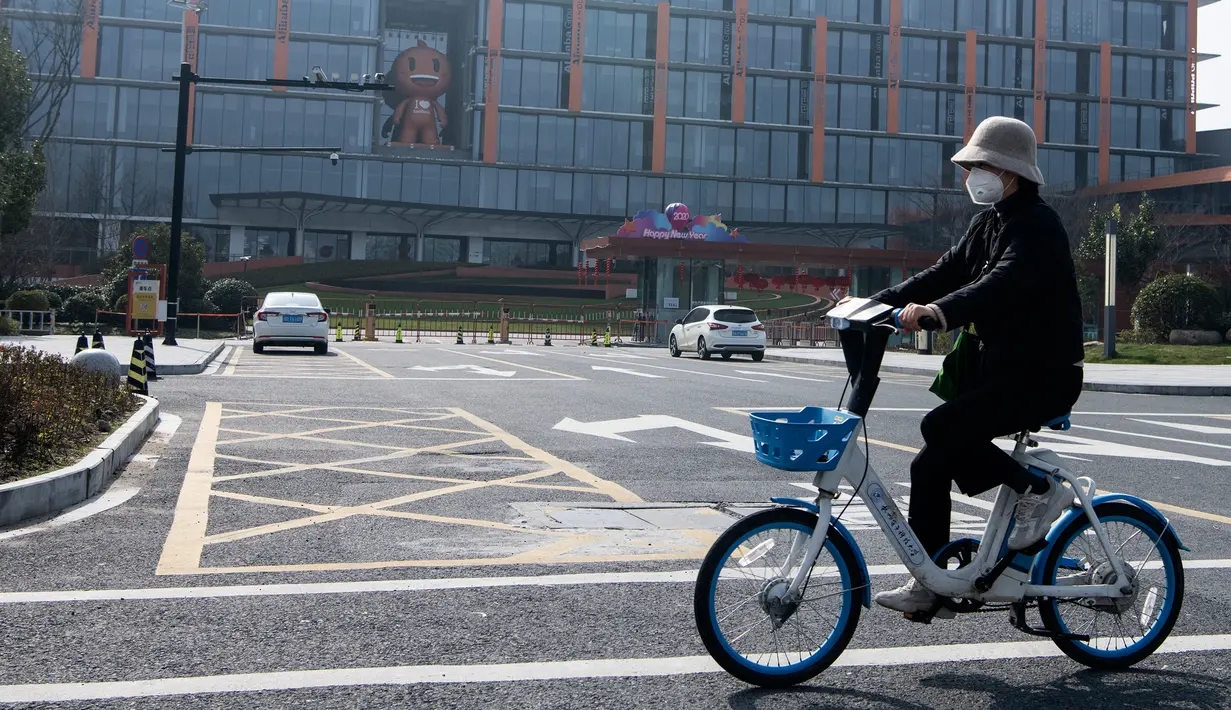 Seorang wanita bermasker mengendarai sepeda di depan kantor pusat Alibaba di Kota Hangzhou, Provinsi Zhejiang, China, Rabu (5/2/2020). Pemerintah Hangzhou memberlakukan pembatasan pergerakan bagi warganya menyusul mewabahnya virus corona. (NOEL CELIS/AFP)