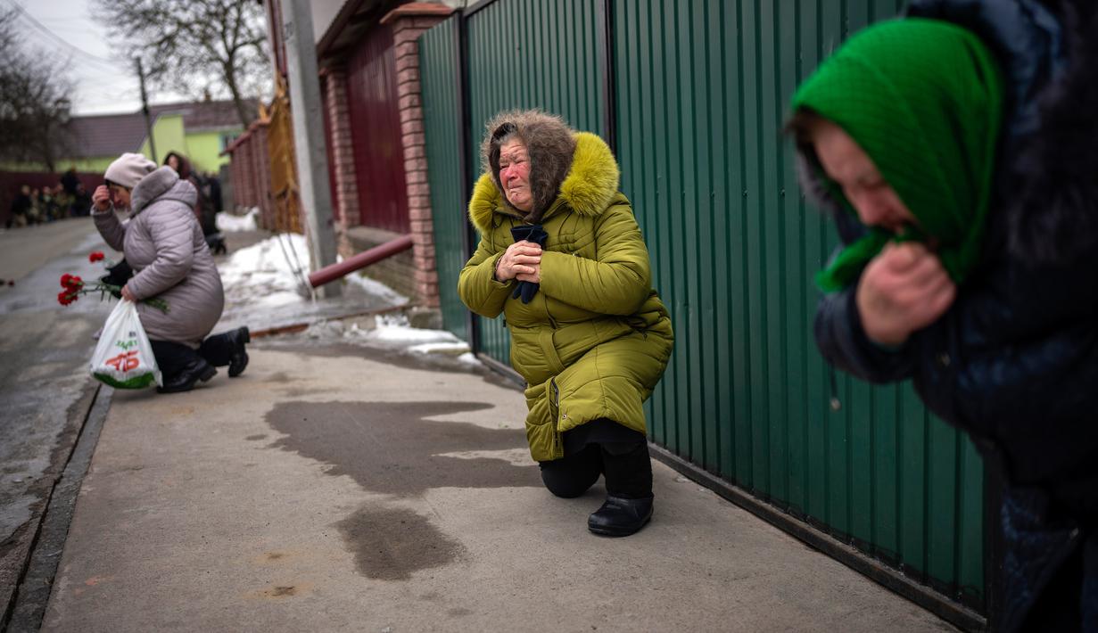 Para pelayat berlutut menunggu peti mati Oleksandr Maksymenko (38) lewat saat pemakamannya di kampung halamannya di Kniazhychi, sebelah timur Kyiv, Ukraina, 13 Februari 2023. Oleksandr Maksymenko, seorang warga sipil yang menjadi sukarelawan di angkatan bersenjata Ukraina, tewas dalam pertempuran di daerah Bakhmut. (AP Photo/Emilio Morenatti)