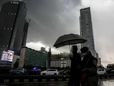 Warga menggunakan payung melintas di kawasan Bundaran Hi, Jakarta, Sabtu (13/11/2021). Badan Meteorologi Klimatologi dan Geofisika (BMKG) melansir peringatan terbaru yang berlaku 7-9 November 2021 soal peringatan cuaca ekstrem imbas dari La Nina. (Liputan6.com/Faizal Fanani)