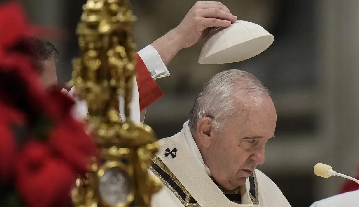 Seorang ajudan melepas topi tengkorak Paus Fransiskus selama Misa Malam Natal, di Basilika Santo Petrus, di Vatikan, Jumat (24/12/2021). Di acara tersebut, Paus Fransiskus mengatakan meskipun ada kebangkitan kasus COVID-19 yang telah mendorong mandat vaksin baru untuk karyawan Vatikan. (AP Photo/Ale