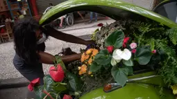 Roberta Machado dari Brasil menata bunga dan tanaman untuk dijual dengan Volkswagen Beetle 1969 yang diubah menjadi toko bunga keliling di Copacabana, Rio de Janeiro, Rabu (14/10/2020). Perempuan 51 tahun ini mengubah VW kodok untuk bertahan dari krisis akibat pandemi COVID-19. (MAURO PIMENTEL/AFP)