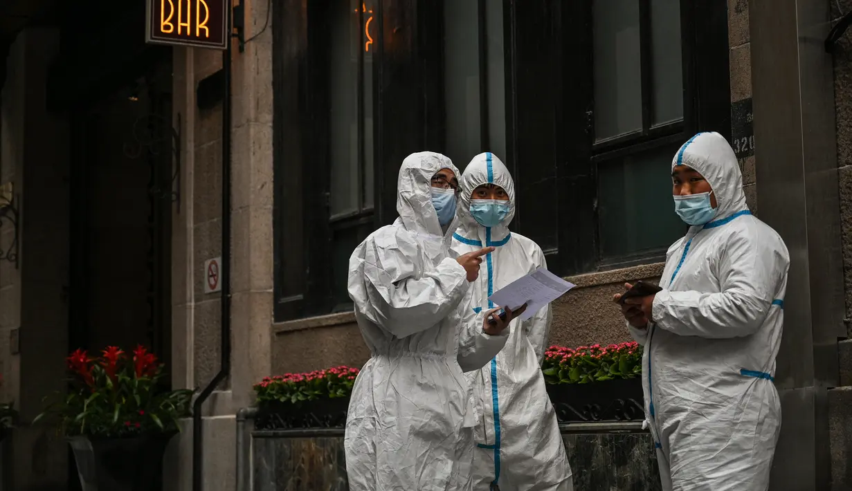Pekerja yang mengenakan alat pelindung diri berdiri di sebelah akses hotel di Bund, Puxi, Shanghai, China, 31 Maret 2022. Daerah Puxi akan lockdown mulai 1 April 2022. (Hector RETAMAL/AFP)