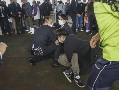Seorang pria (di tanah) yang melemparkan apa yang tampak seperti bom asap, ditangkap di sebuah pelabuhan di Wakayama, Jepang barat, Sabtu (15/4/2023). (Kyodo News via AP)