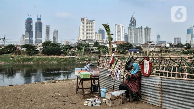 Pedagang berjualan makanan ringan di bantaran Kanal Banjir Barat dengan latar belakang gedung pencakar langit di Jakarta, Kamis (6/8/2020). BPS mencatat pertumbuhan ekonomi Indonesia Kuartal II/2020 minus 5,32 persen akibat perlambatan sejak adanya pandemi COVID-19. (merdeka.com/Iqbal S. Nugroho)