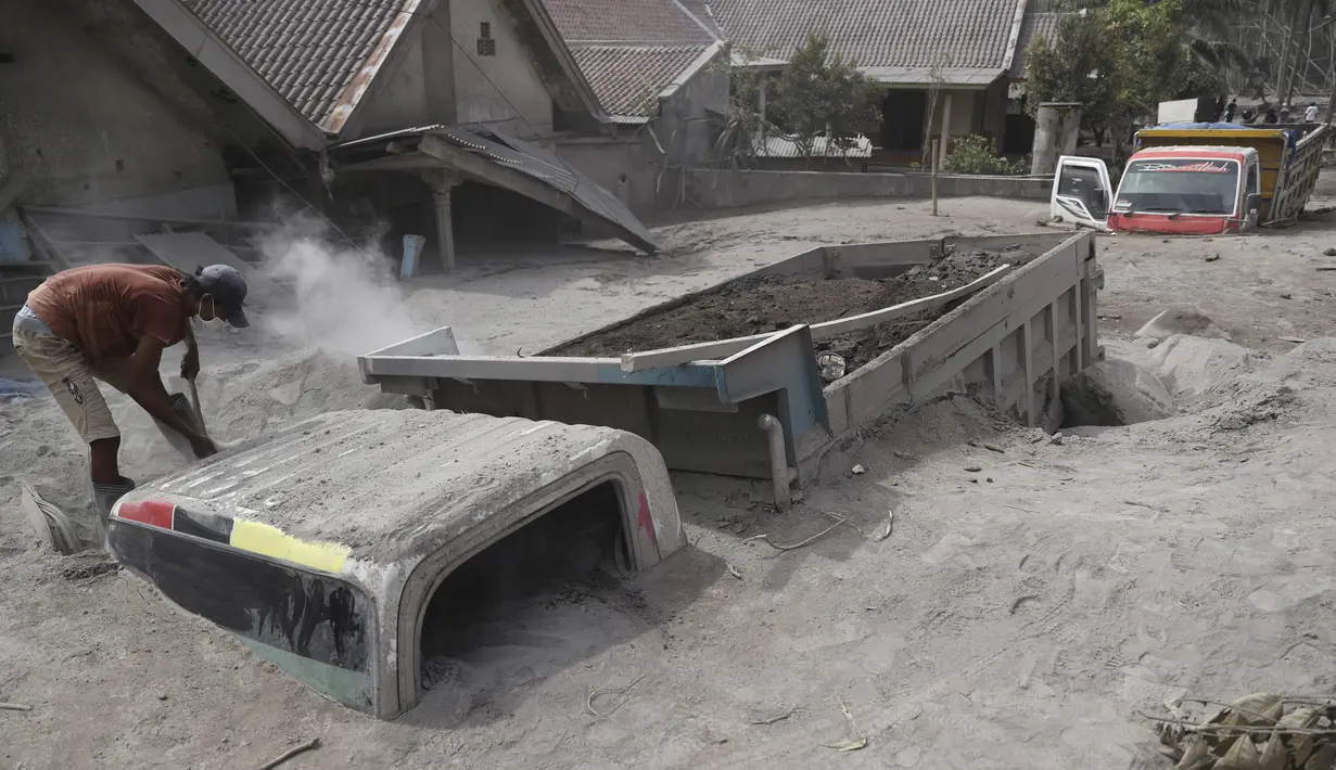 Seorang pria memeriksa truk yang tertimbun abu vulkanik pascaerupsi Gunung Semeru di Lumajang, Jawa Timur, 5 Desember 2021. Tiga jenazah ditemukan di dalam truk pasir yang terjebak erupsi Gunung Semeru.  (AP Photo/Trisnadi)
