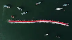 Foto udara memperlihatkan 145 perenang membentangkan bendera Merah Putih sepanjang 78 meter untuk menyambut Hari Ulang Tahun (HUT) ke-78 Republik Indonesia (RI) di perairan Makassar, Sulawesi Selatan, Sabtu (12/8/2023). (Muchtamir ZAIDE/AFP)