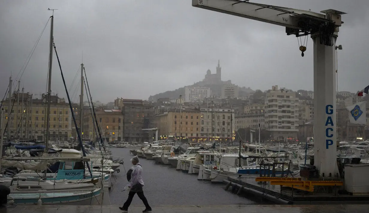 Seorang wanita berjalan di tengah hujan di Pelabuhan Vieux saat badai di Marseille, Prancis selatan, Senin (4/10/2021). Wilayah Prancis selatan dalam siaga untuk hujan lebat dan banjir. (AP Photo/Daniel Cole)