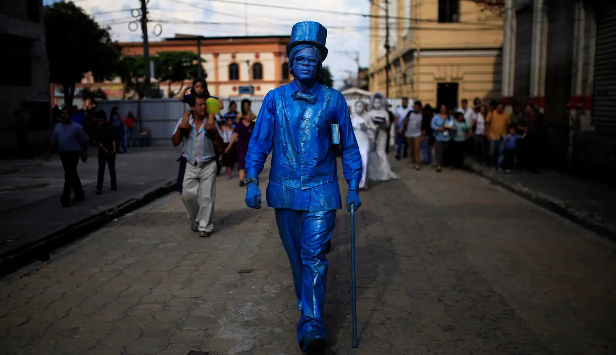 Seorang kontestan beraksi saat mengikuti kontes patung di pusat kota San Salvador , El Salvador, (18/6). Dengan mengecat seluruh tubuh mereka seperti patung, kita akan dibuat sulit membedakan mana patung asli dan tidak. (REUTERS / Jose Cabezas)