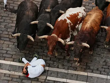 Seorang pengunjung festival terjatuh di depan banteng-banteng aduan Victoriano del Río saat acara lari banteng ketiga di festival San Fermín di Pamplona, Spanyol, Kamis, 9 Juli 2026. (AP Photo/Miguel Oses)