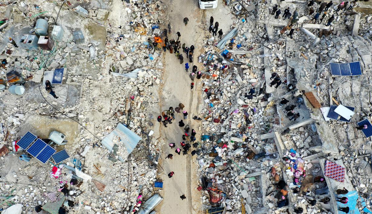 Pemandangan dari udara ini menunjukkan penduduk mencari korban dan penyintas di tengah puing-puing bangunan yang runtuh setelah gempa bumi di desa Besnia dekat Harim, di provinsi Idlib barat laut yang dikuasai pemberontak Suriah di perbatasan dengan Turki, Senin (6/2/2023). Ratusan orang dilaporkan tewas di Suriah utara setelah gempa berkekuatan 7,8 yang berasal dari Turki dan dirasakan di seluruh negara tetangga. (Omar HAJ KADOUR / AFP)