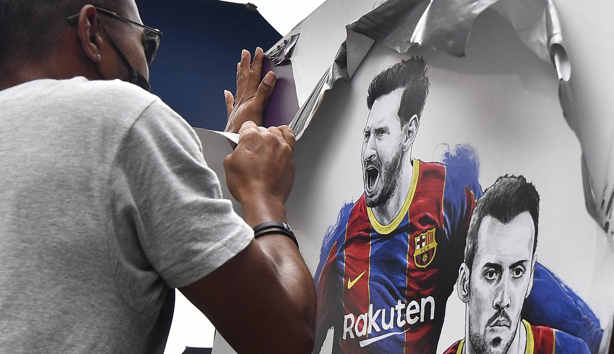 Seorang pekerja melepas poster-poster yang menampilkan pemain depan Barcelona Lionel Messi di stadion Camp Nou di Barcelona (10/8/2021). Prancis menunggu dengan tidak sabar Lionel Messi dengan para pendukung berkumpul di luar lapangan Paris Saint-Germain. (AFP/ Pau Barrena)