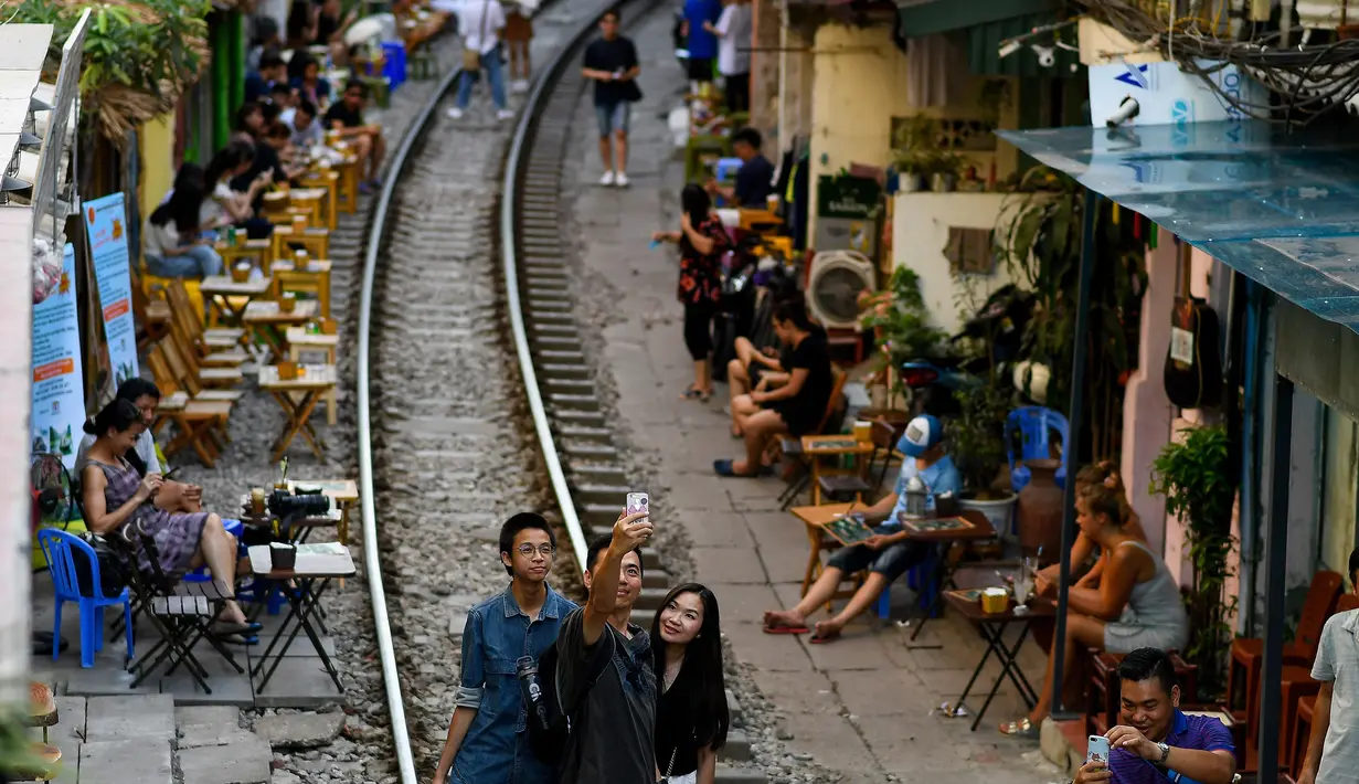 Foto pada 8 Juni 2019 memperlihatkan wisatawan berswafoto di tengah jalur kereta api populer di Hanoi. Di ibu kota Vietnam tersebut rel-rel kereta yang berada di permukiman padat penduduk dijadikan destinasi wisata selfie. (Photo by Manan VATSYAYANA / AFP)