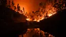 Kobaran api dari kebakaran hutan terpantul dari air di Penela, Portugal Tengah, Minggu (18/6). Setidaknya 25 orang tewas pada kebakaran hutan di Portugal, sebagian akibat terperangkap dalam mobil ketika api melalap hutan. (PATRICIA DE MELO MOREIRA/AFP)