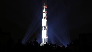 Orang-orang menyaksikan proyeksi roket NASA, Saturn V, di Monumen Washington menandai peringatan 50 tahun misi Apollo 11 ke bulan di National Mall, Washington, Selasa (16/7/2019). Pada 16 Juli 1969, NASA mencatatkan sejarah dengan melakukan peluncuran Apollo 11. (Mark Wilson/Getty Images/AFP)
