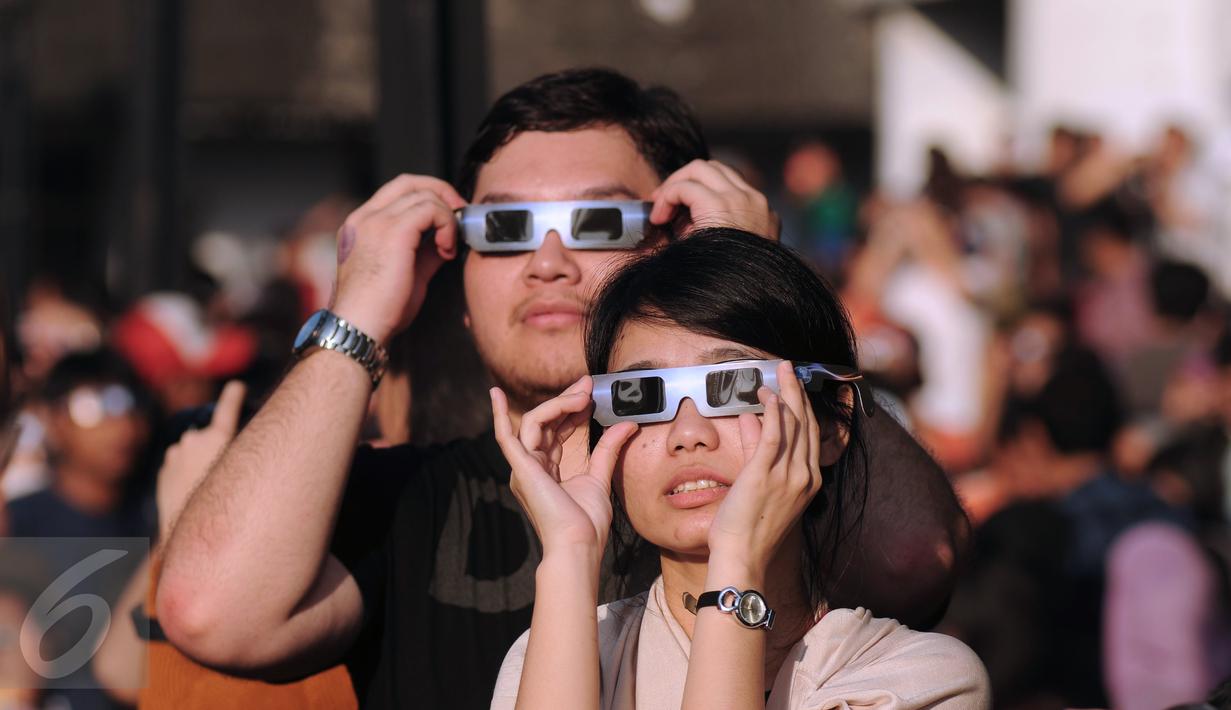 Sepasang muda mudi menggunakan kacamata khusus untuk melihat proses gerhana matahari di sekitar Taman Ismail Marzuki, Jakarta, Rabu (9/3/2016). Di Jakarta, fenomena gerhana matahari 90% bisa diamati selama 2,11 menit. (Liputan6.com/Helmi Fithriansyah)   