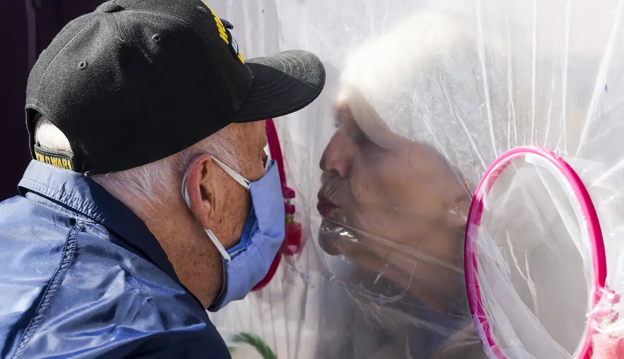 Betty Van Putten (kanan) bergerak untuk mencium suaminya melalui tenda pelukan di komunitas Crossroads Senior Living di Lakewood, Colorado, Jumat (26/2/2021). Tenda dengan penghalang plastik memungkinkan anggota keluarga terhubung secara fisik satu sama lain. (Michael Ciaglo/Getty Images/AFP)